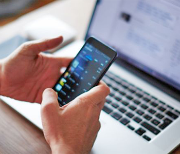 hands holding a smart phone with a picture of a laptop in the background