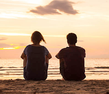 a teen boy and girl on the beach looking out at the ocean